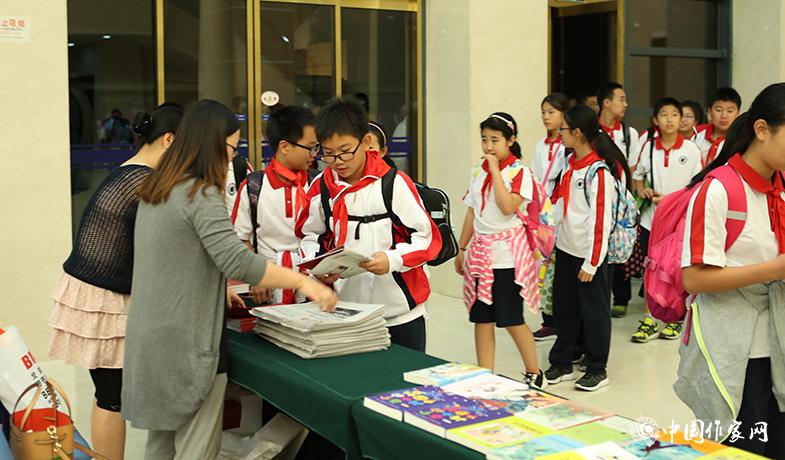 參加頒獎典禮的學生排隊入場，工作人員為他們分發(fā)當天的《文藝報》兒獎特刊